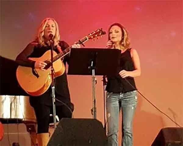 Two women are singing and playing guitars on a stage.