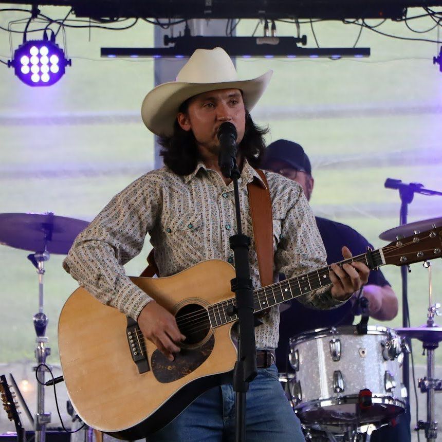 A man in a cowboy hat is singing into a microphone while holding a guitar