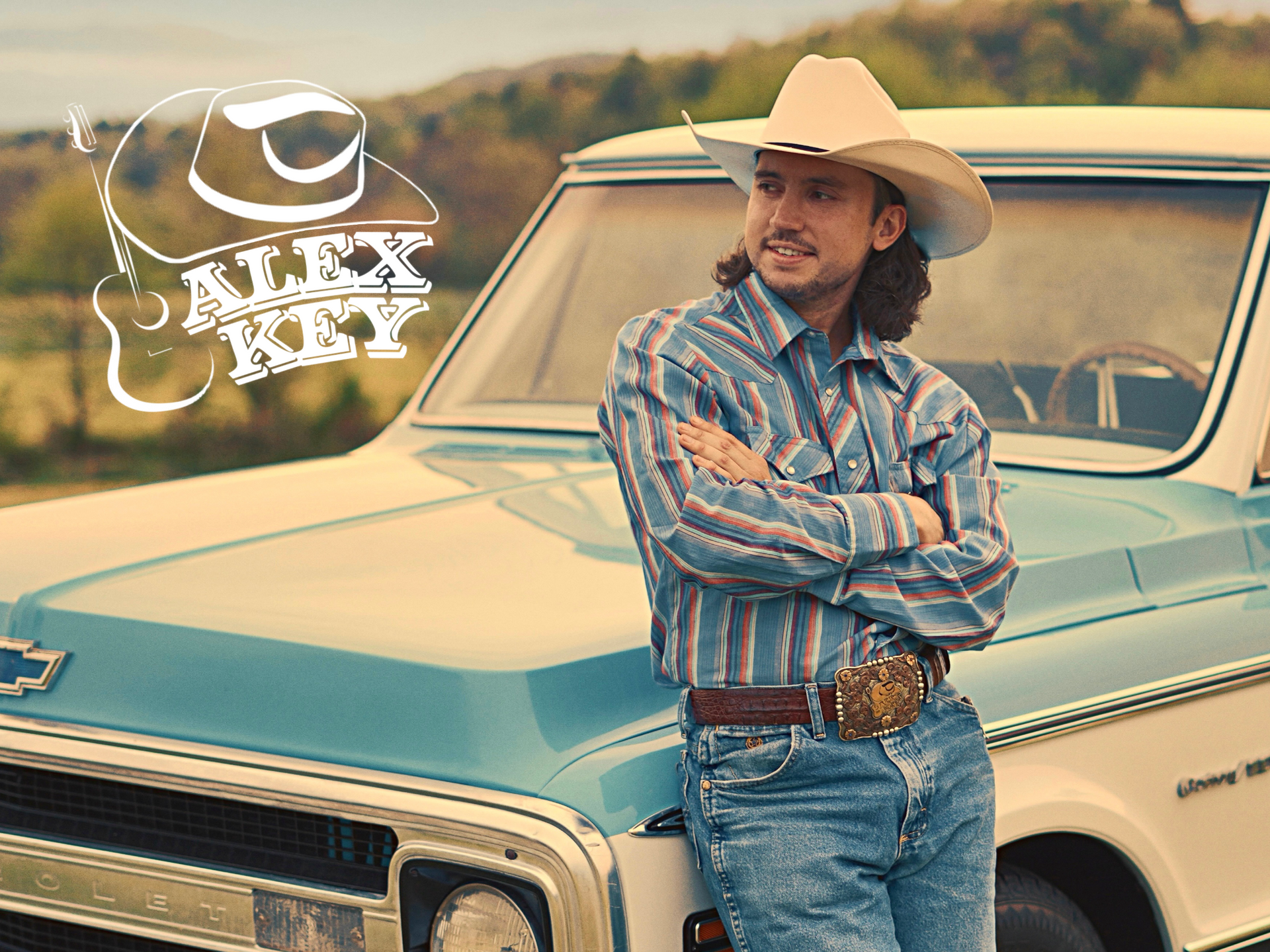 A man in a cowboy hat is leaning against a blue truck.