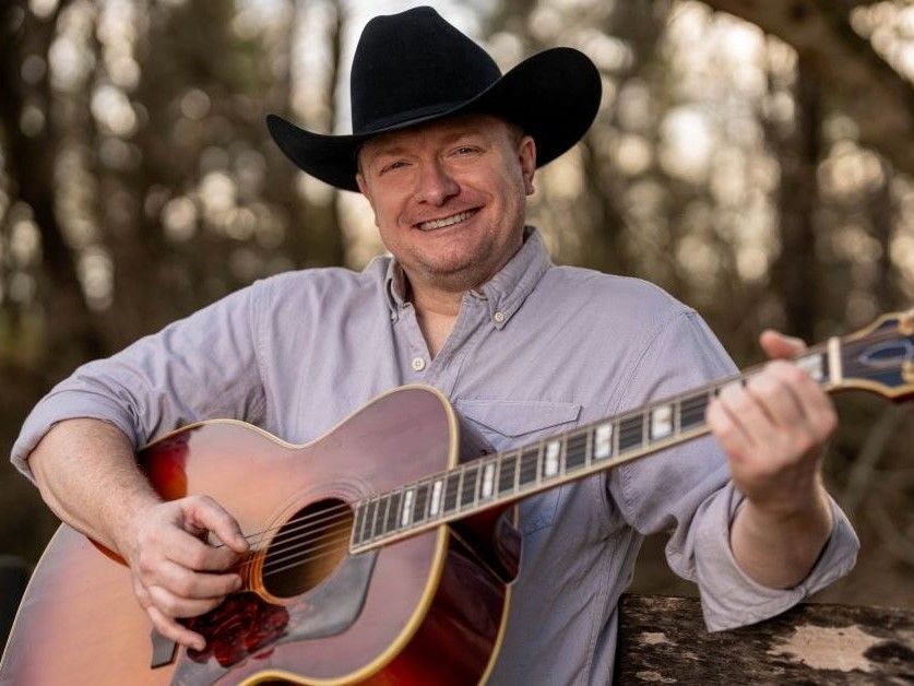 A man in a cowboy hat is holding an acoustic guitar.