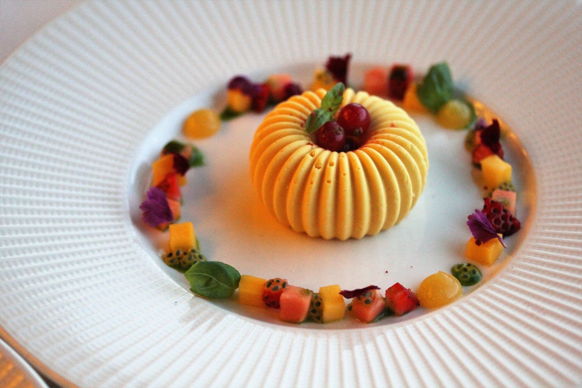 A white plate topped with a yellow dessert and fruit.