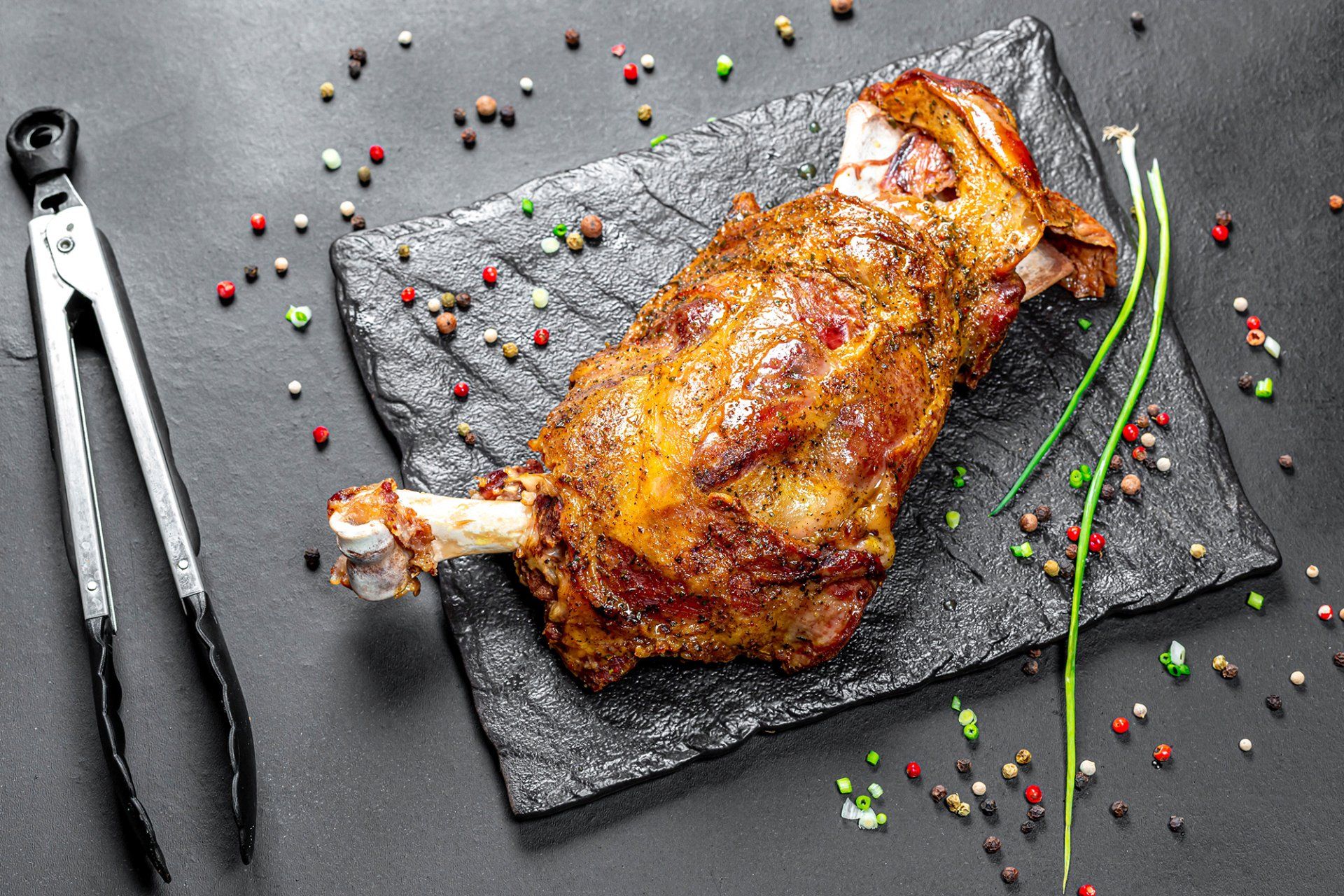 A piece of meat is sitting on a cutting board next to tongs.