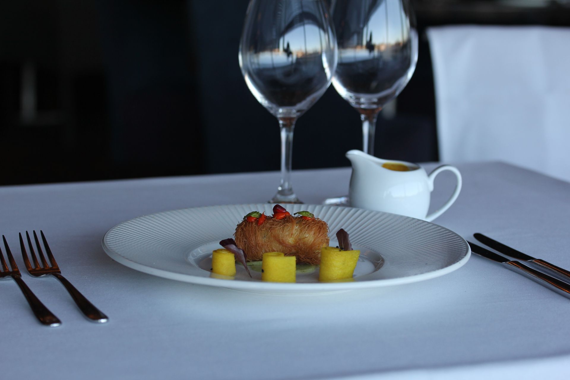 A plate of food sits on a table next to wine glasses