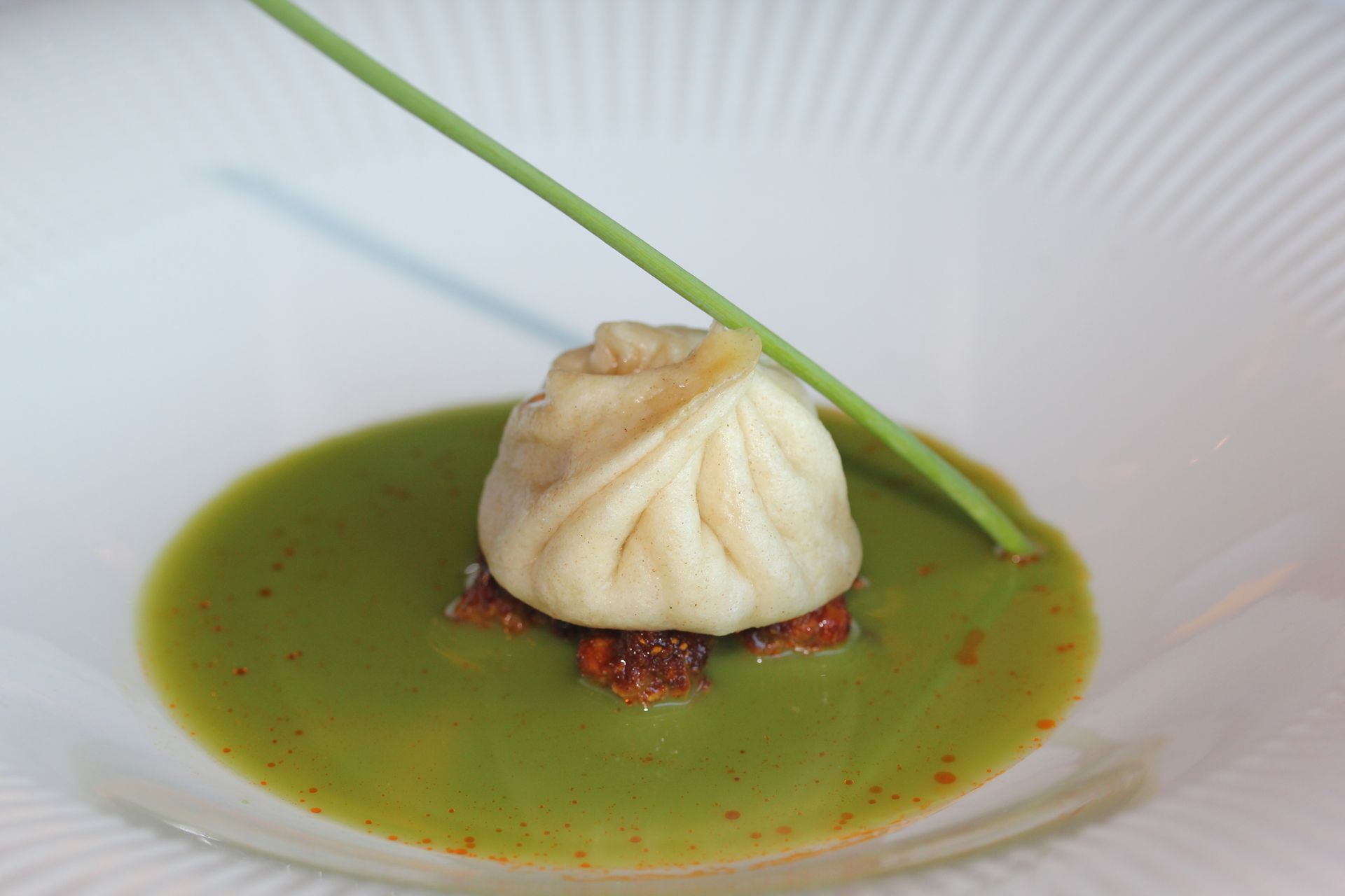 A close up of a plate of food with a green sauce and a dumpling on top.