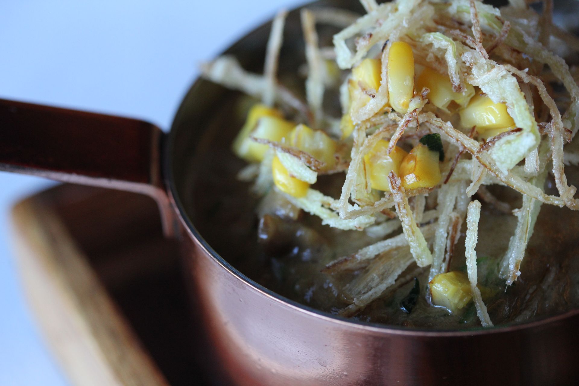 A close up of a pot of food with noodles and corn on a table.