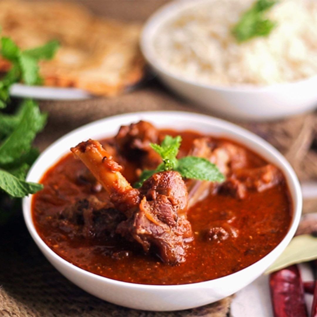 A bowl of chicken stew with rice in the background