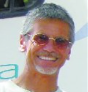 A man wearing sunglasses and a white shirt is smiling for the camera.