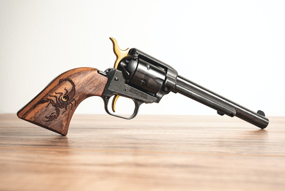 A revolver with a wooden grip is sitting on a wooden table.