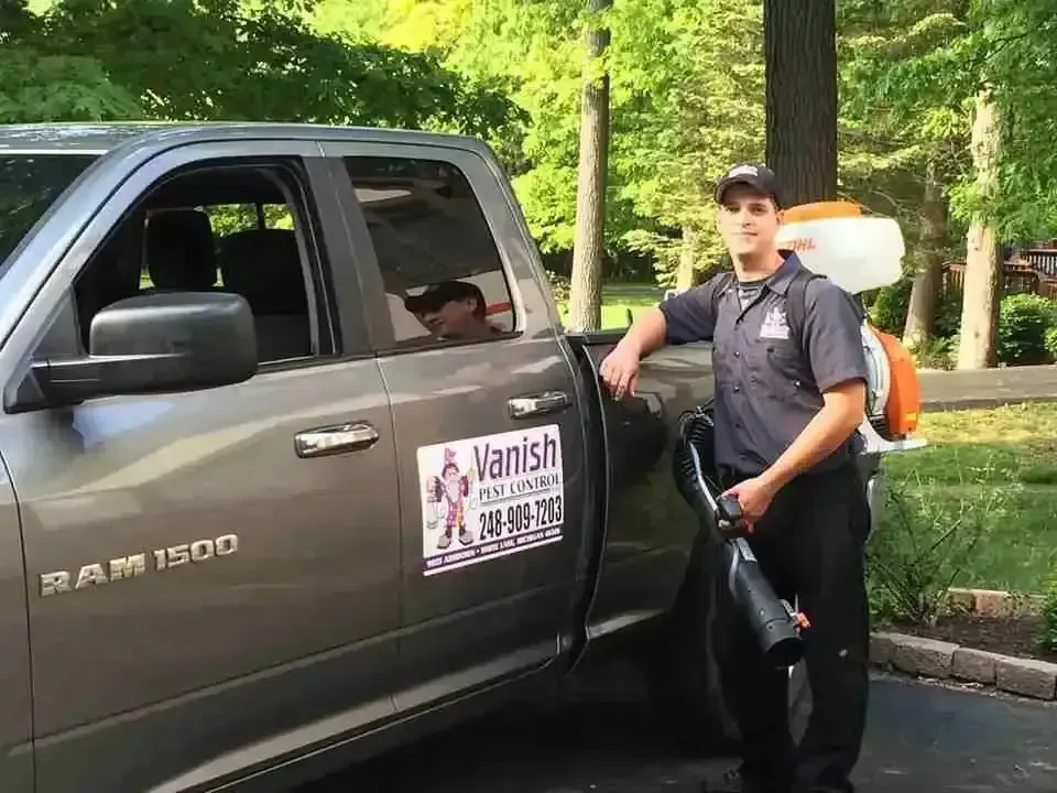 Man in uniform with a fogger, next to a truck. 