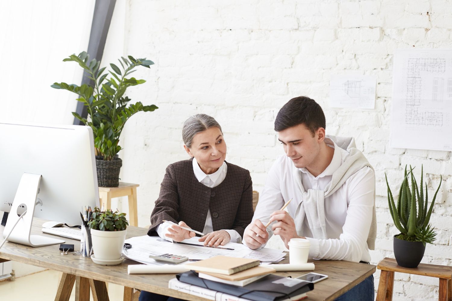 Woman and man reviewing documents at a desk in an office with plants and a computer.