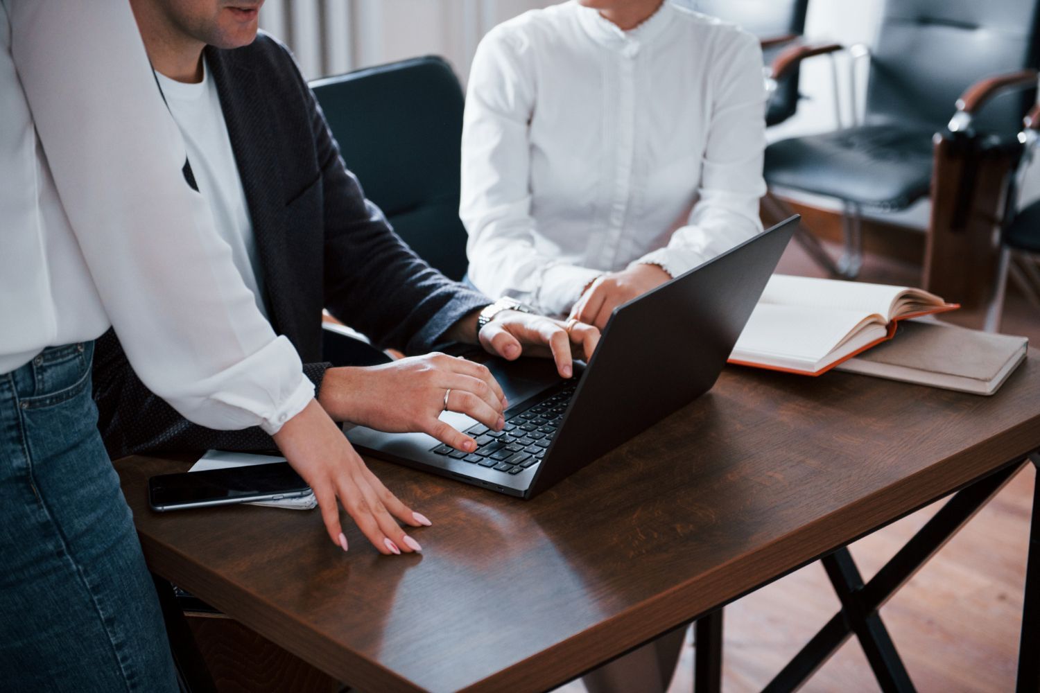 Three people around a desk, looking at a laptop. One person types; two others are observing.