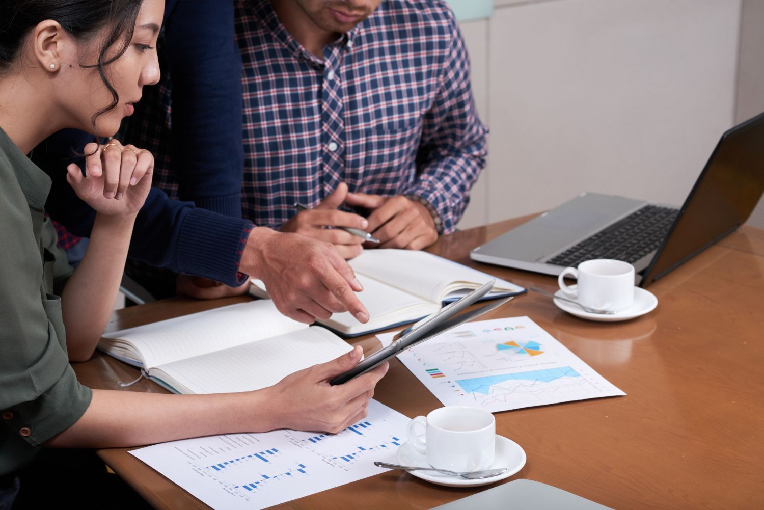 People reviewing documents and data at a table with laptop, notebooks, and coffee cups.