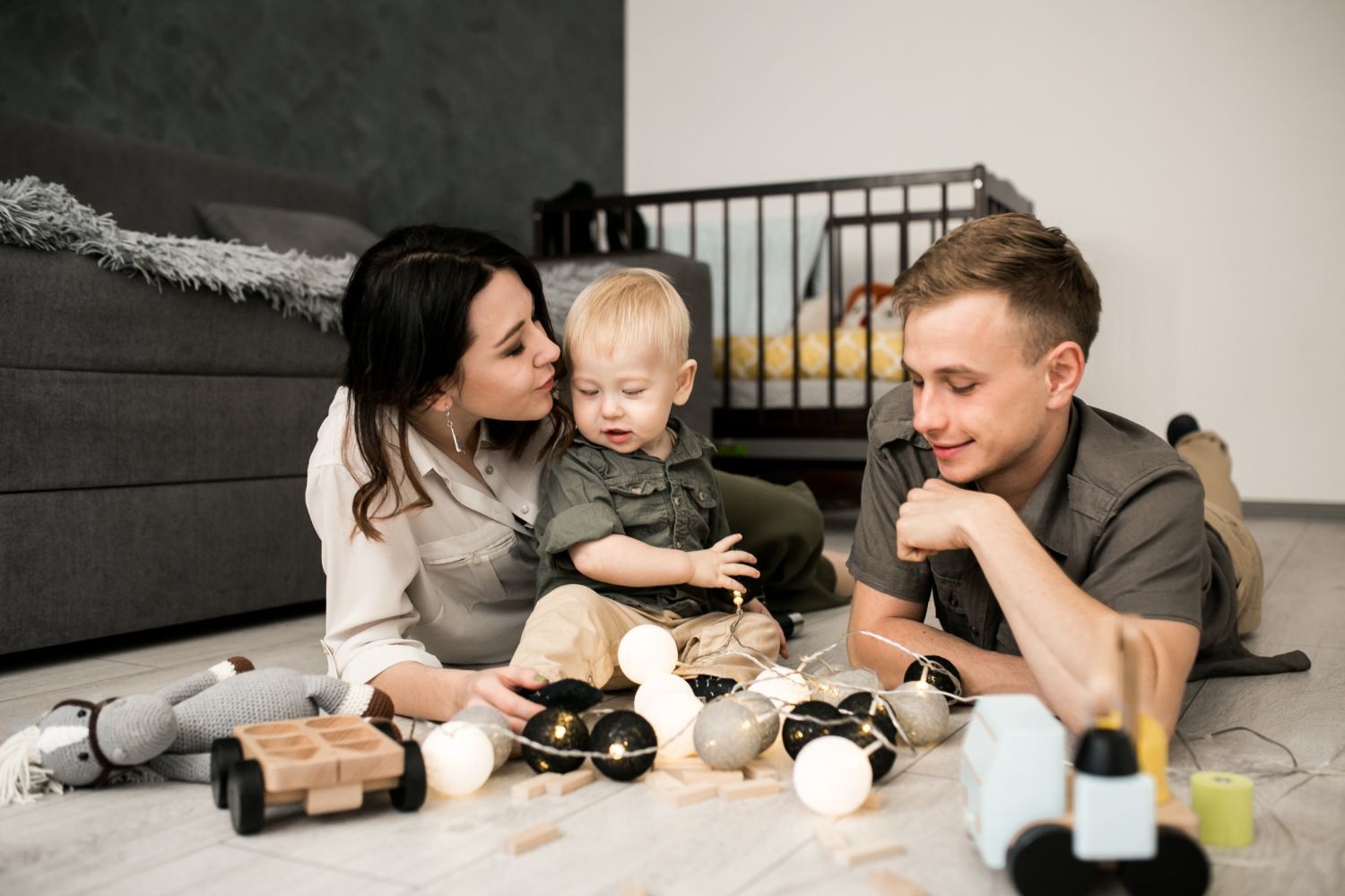 Family of three laying on floor playing with toys.