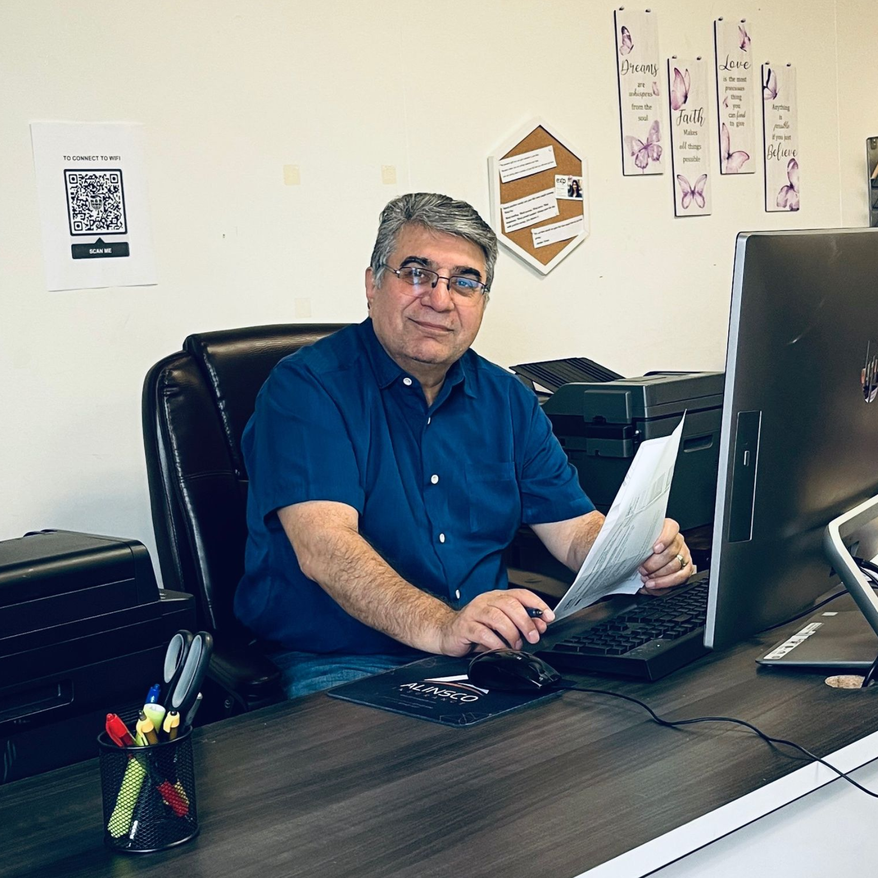 Woman at desk in office, smiling, with a computer and tax documents in the background.