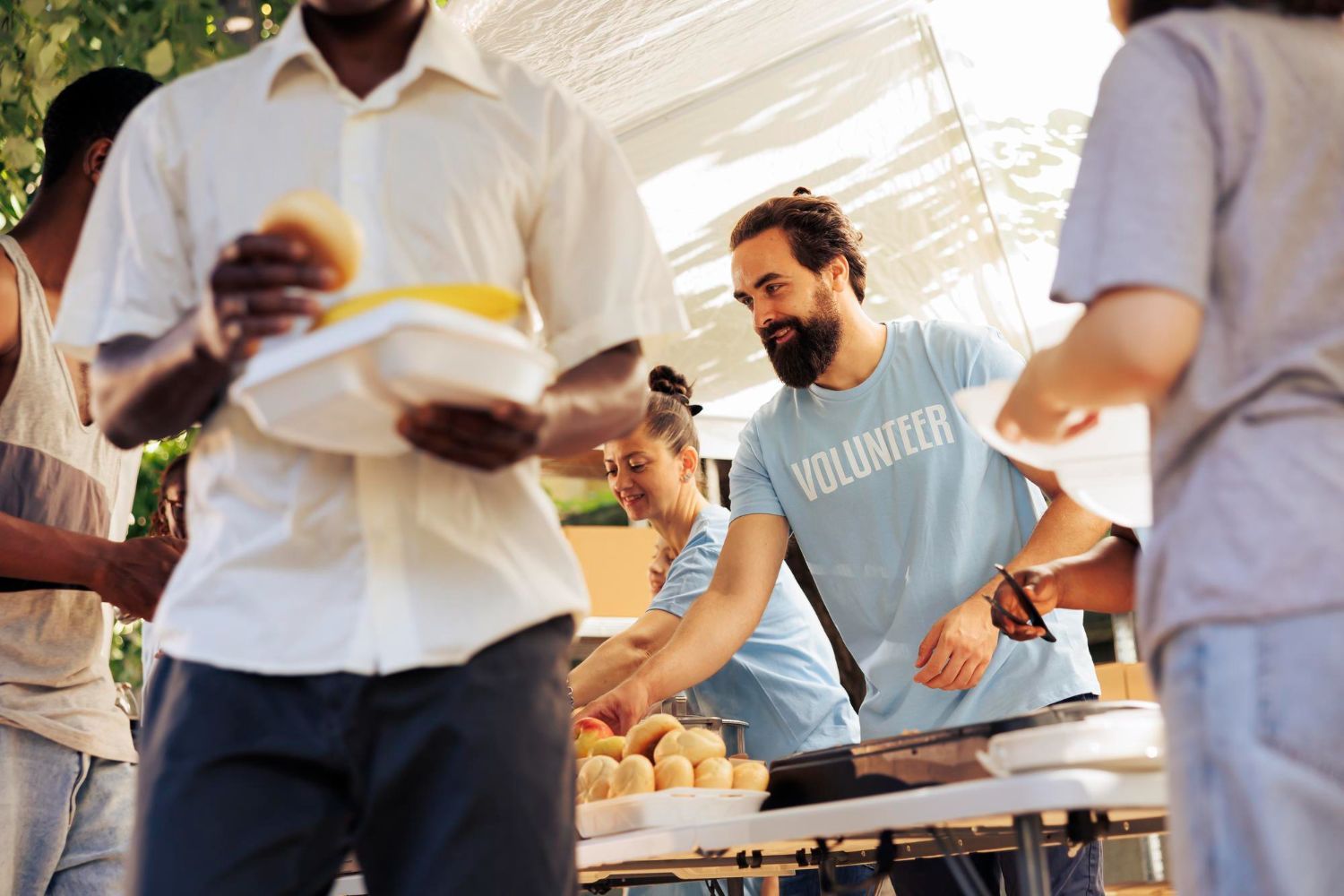 Volunteers serving food at an outdoor event. People holding plates, smiling, and wearing