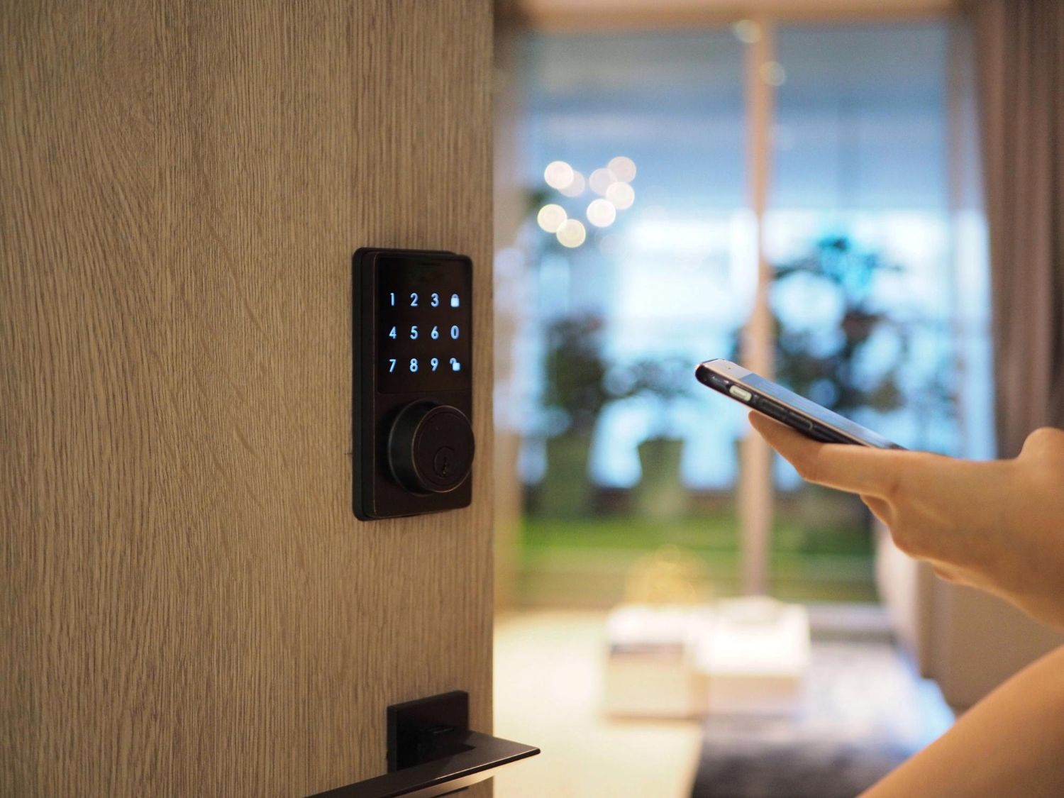 Person unlocking smart lock with phone; keypad and door visible.