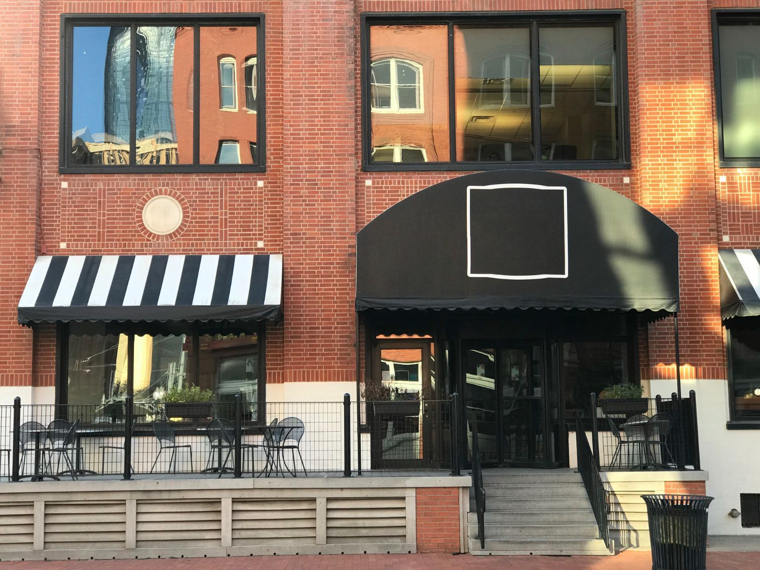 Brick building with black awning and striped awning over restaurant entrance. Windows reflect other buildings.