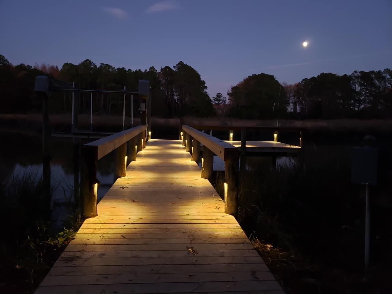 A dock is lit up at night with a full moon in the background 
