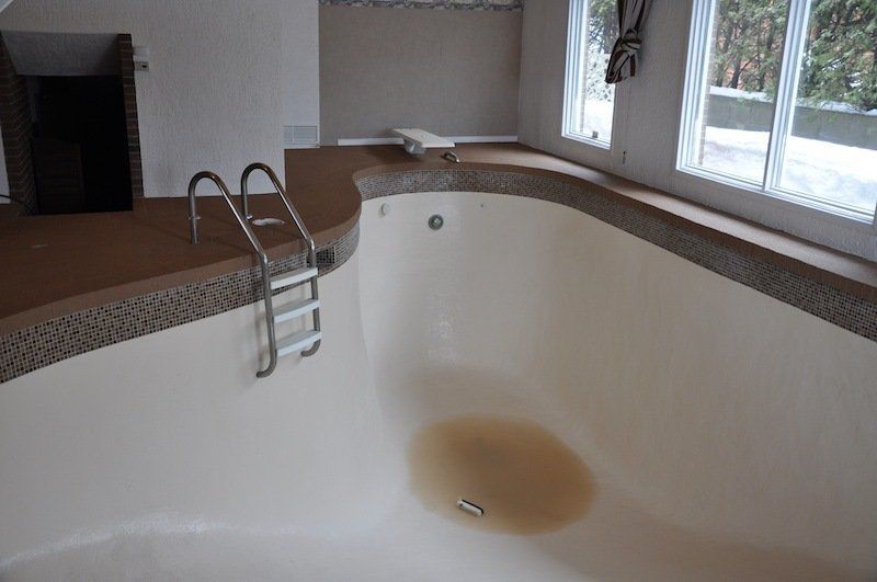 Une piscine avec des escaliers et une tache brune au milieu