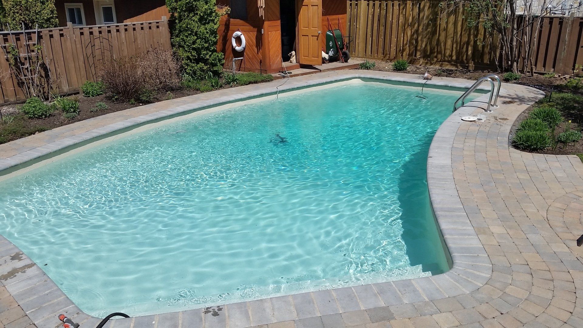 Une grande piscine est entourée d'un patio en briques et d'une clôture en bois.