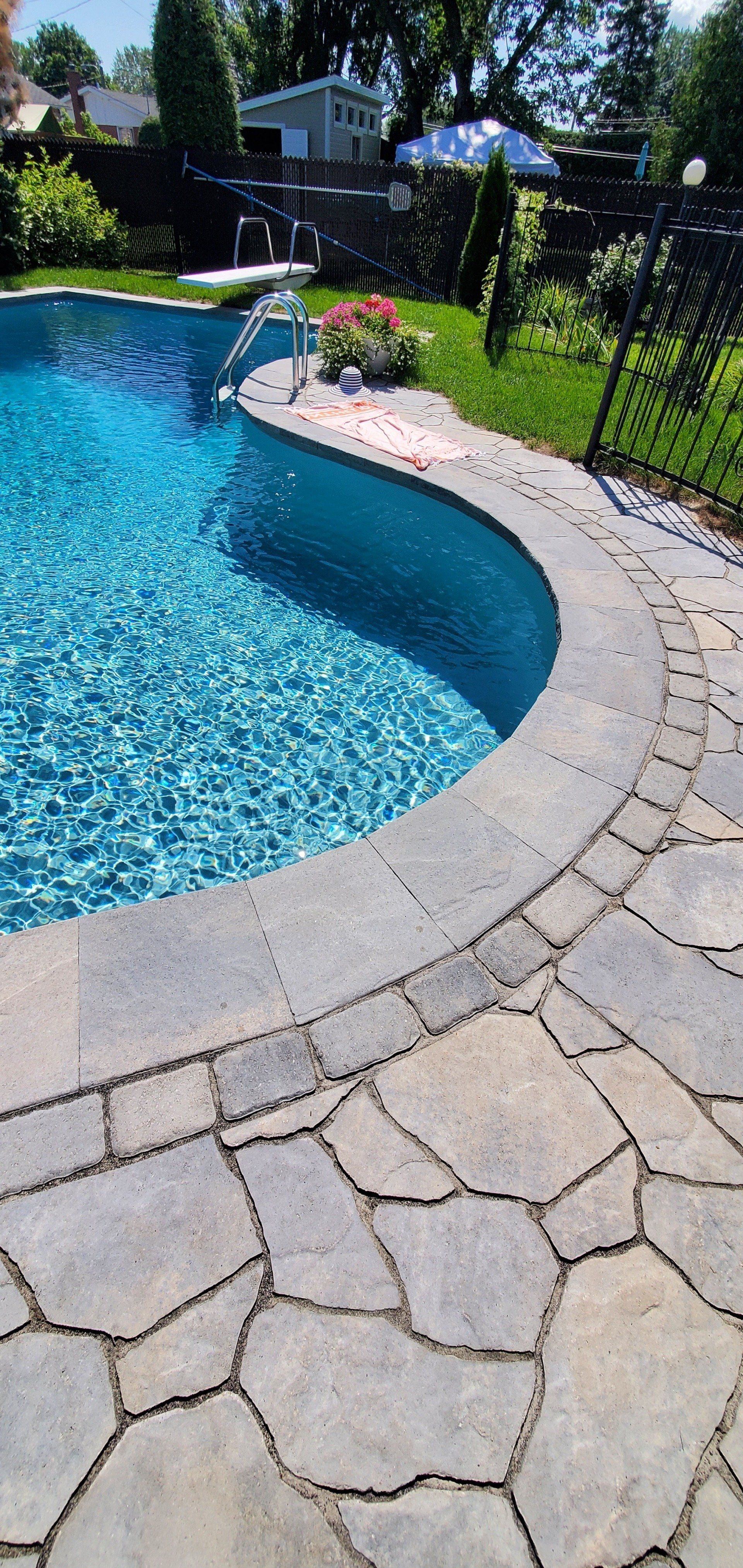 Une piscine à l'eau bleue et un patio en pierre, avec une végétation luxuriante en arrière-plan.