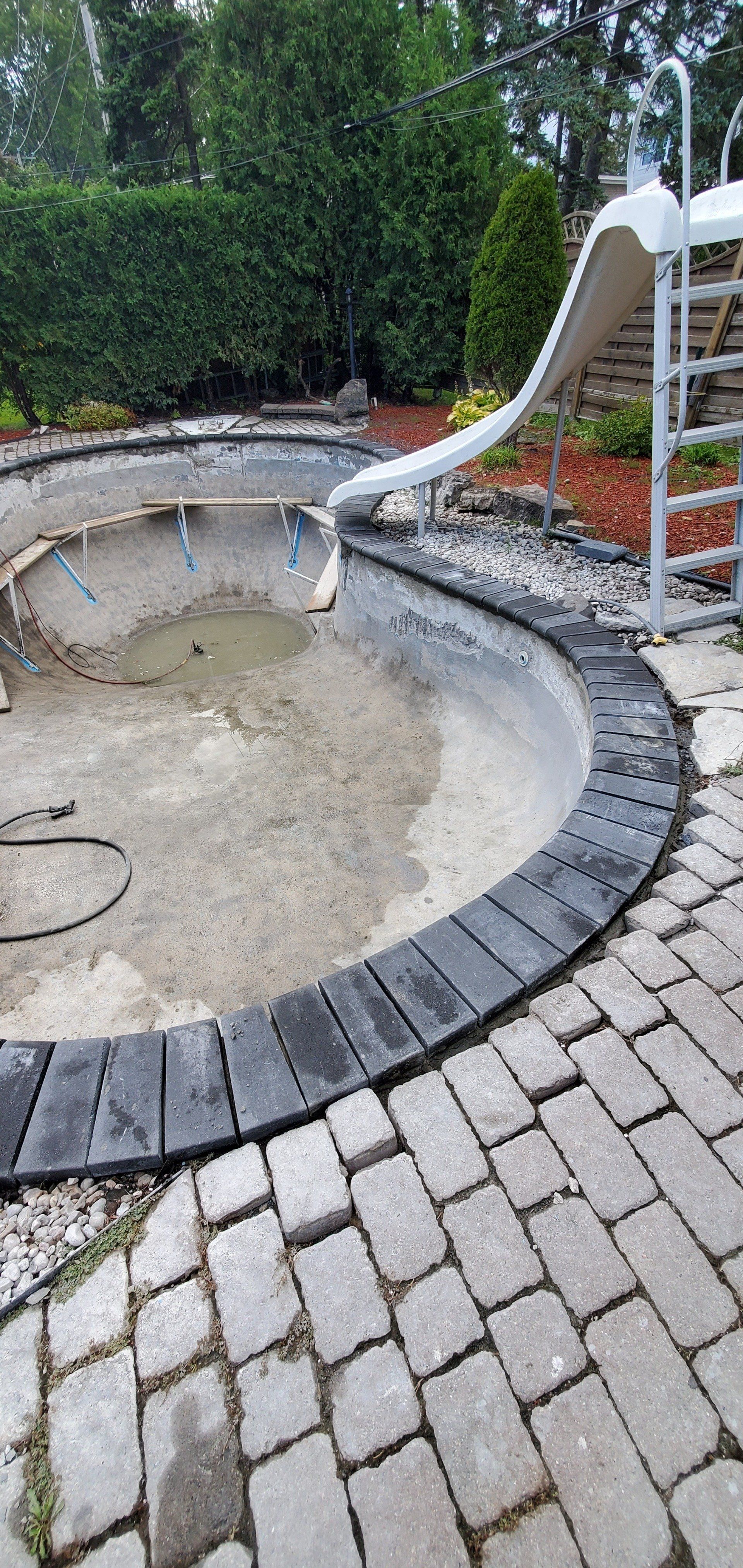 Une piscine est en cours de rénovation avec un toboggan et des escaliers.