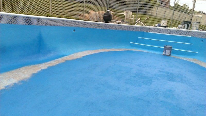 Une piscine bleue avec des escaliers et une clôture en arrière-plan.