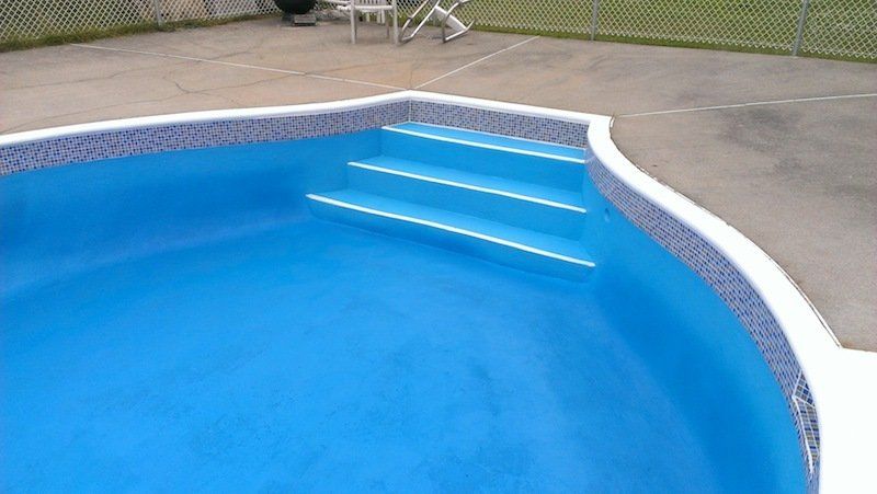 Une piscine bleue avec des escaliers et une clôture en arrière-plan.