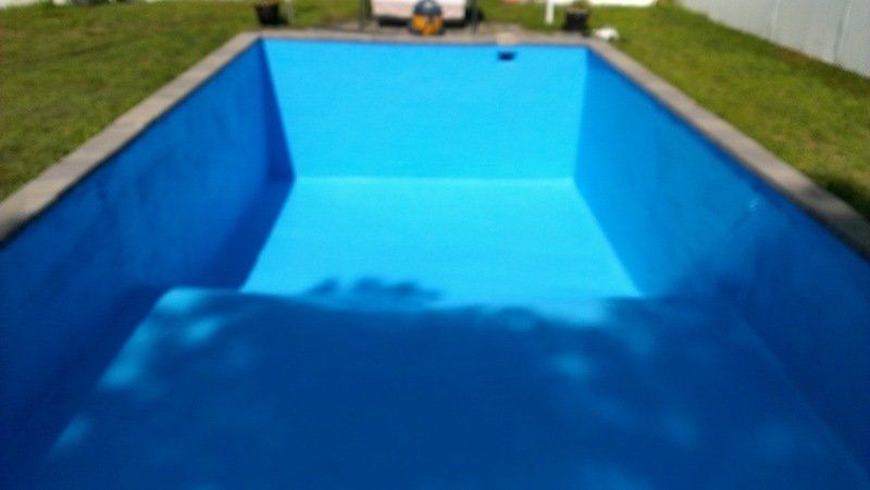 Une piscine bleue est vide et entourée d'herbe.
