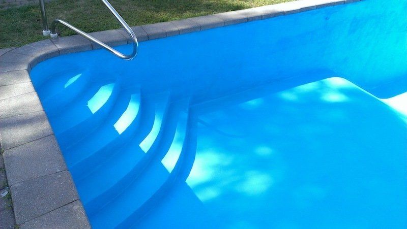 Piscine peinte en bleu avec marches intégrées et rampe métallique le long du bord, aménagement extérieur.