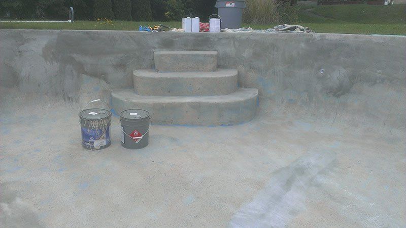 Deux seaux de peinture sont posés sur une surface en béton à côté des escaliers.