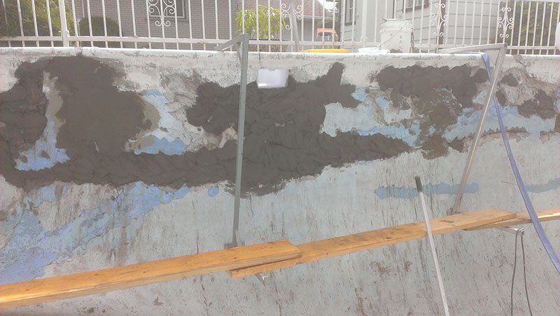 Un mur en béton avec une clôture en arrière-plan et une planche de bois au premier plan.