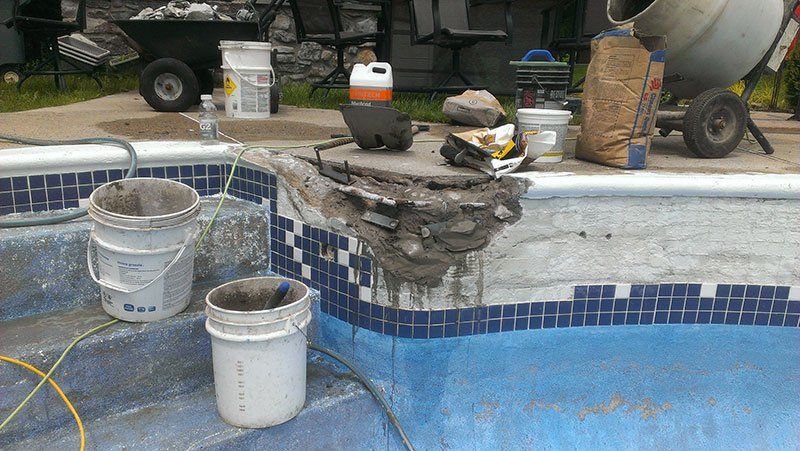 Des seaux de ciment sont posés sur le bord d'une piscine.