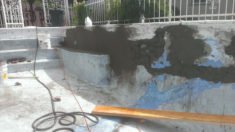 Une piscine est en cours de rénovation avec du béton et une planche de bois.