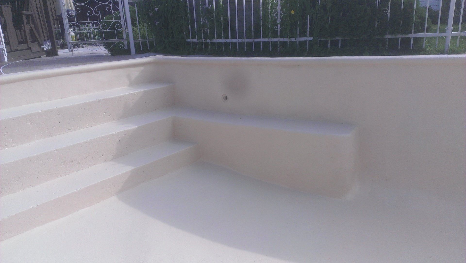 Escalier de piscine beige menant à une piscine beige. Une balustrade blanche est visible.