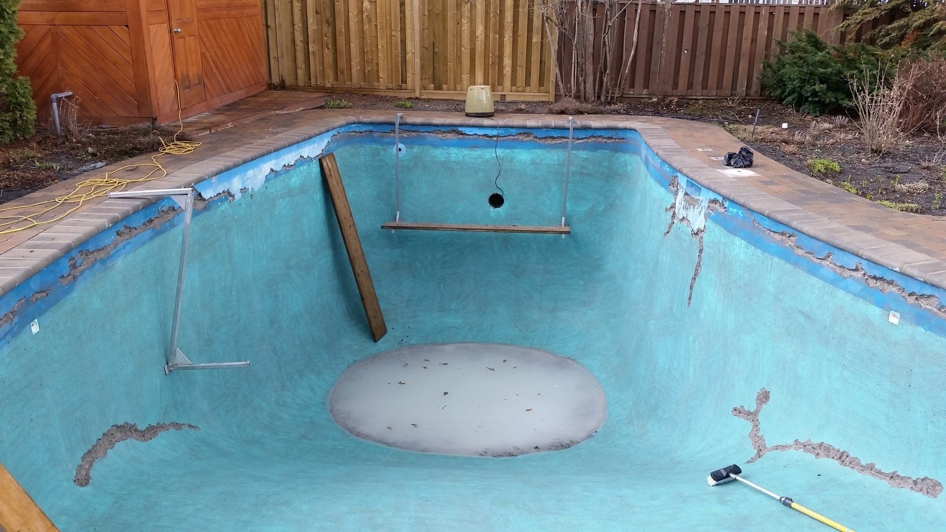 Une piscine vide avec une clôture en bois en arrière-plan.