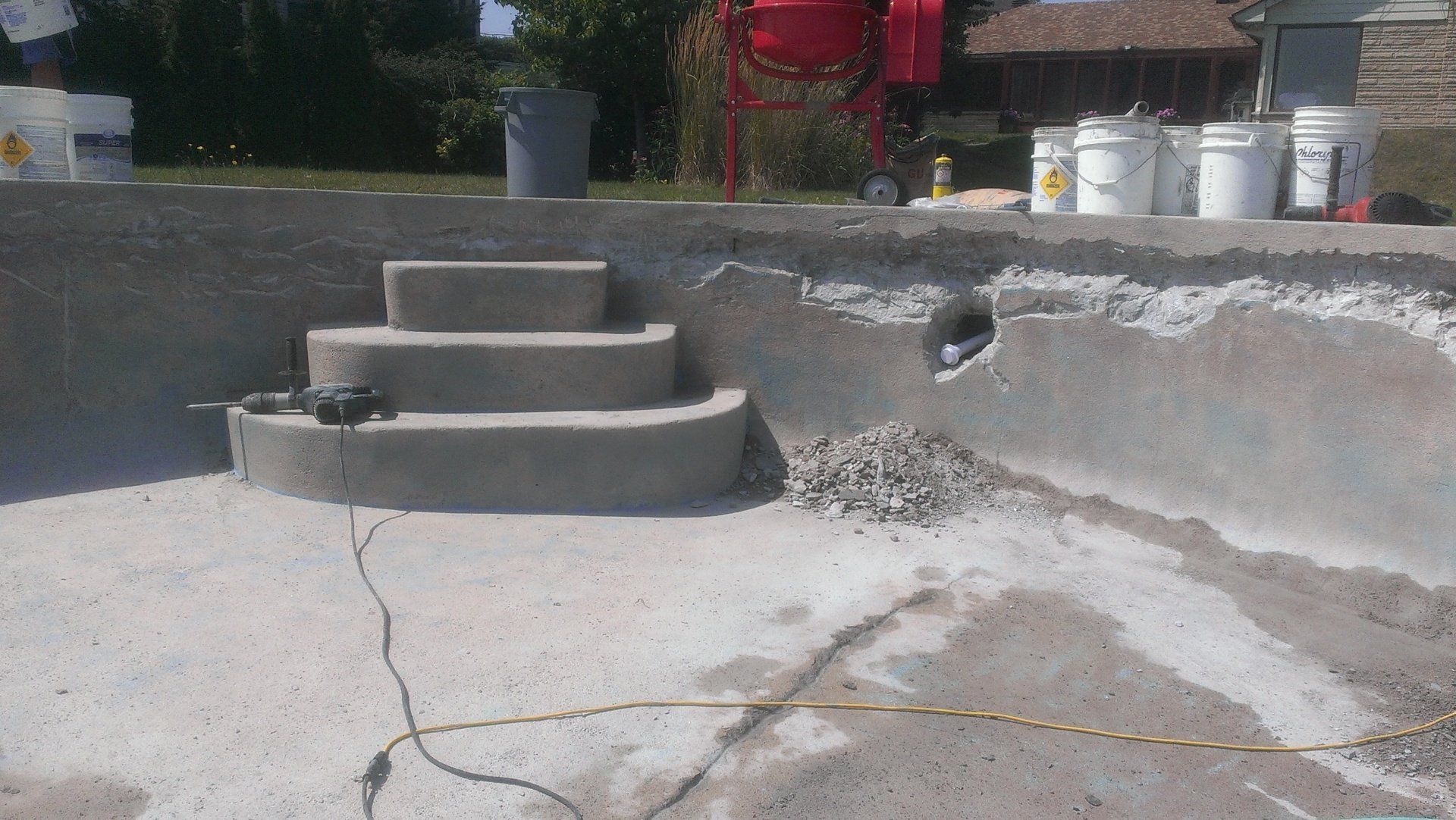 Une piscine est en cours de rénovation avec des escaliers et des seaux de peinture.