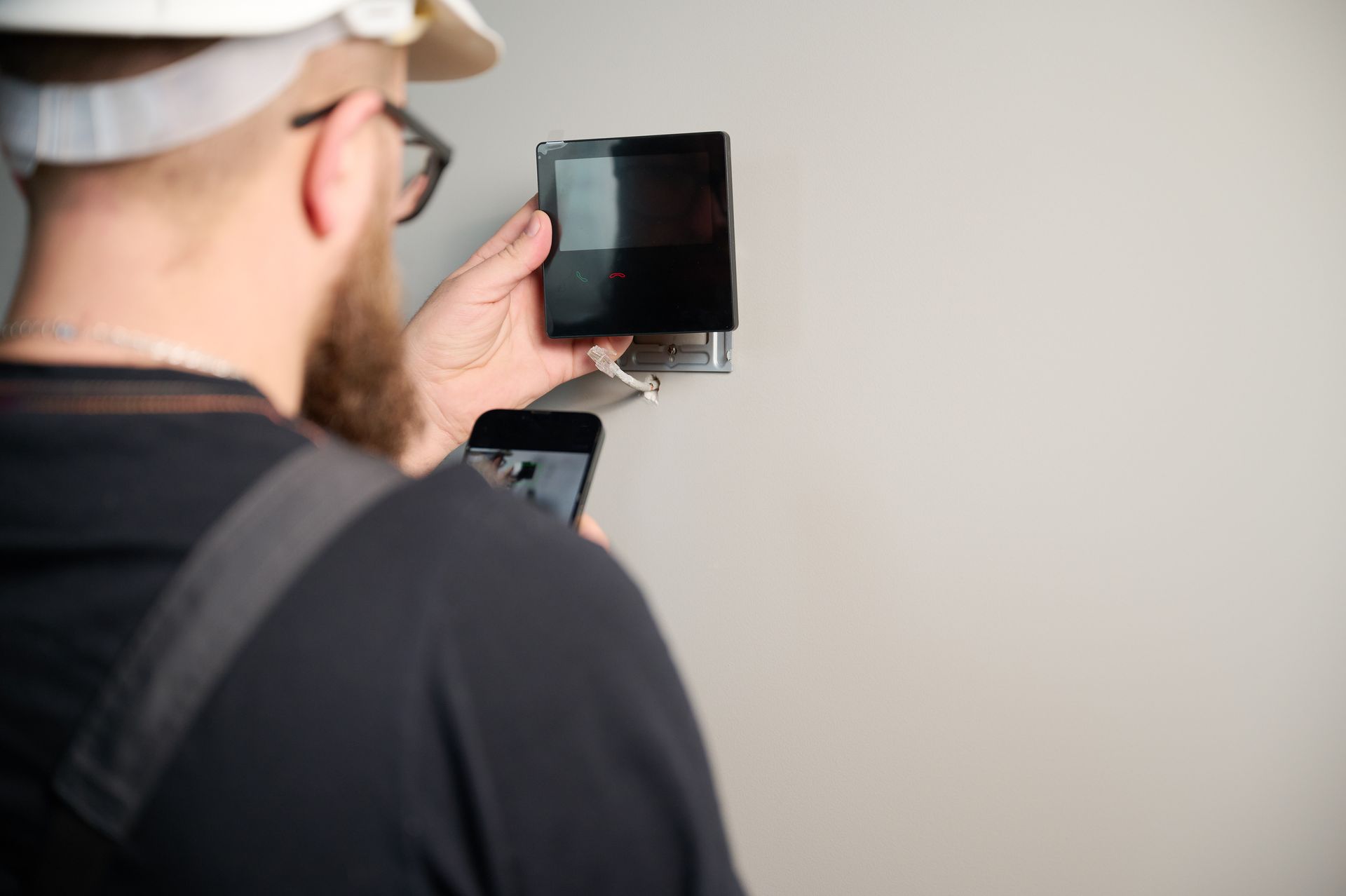 Person using a smartphone to inspect a wall-mounted black device while holding a brush or roller