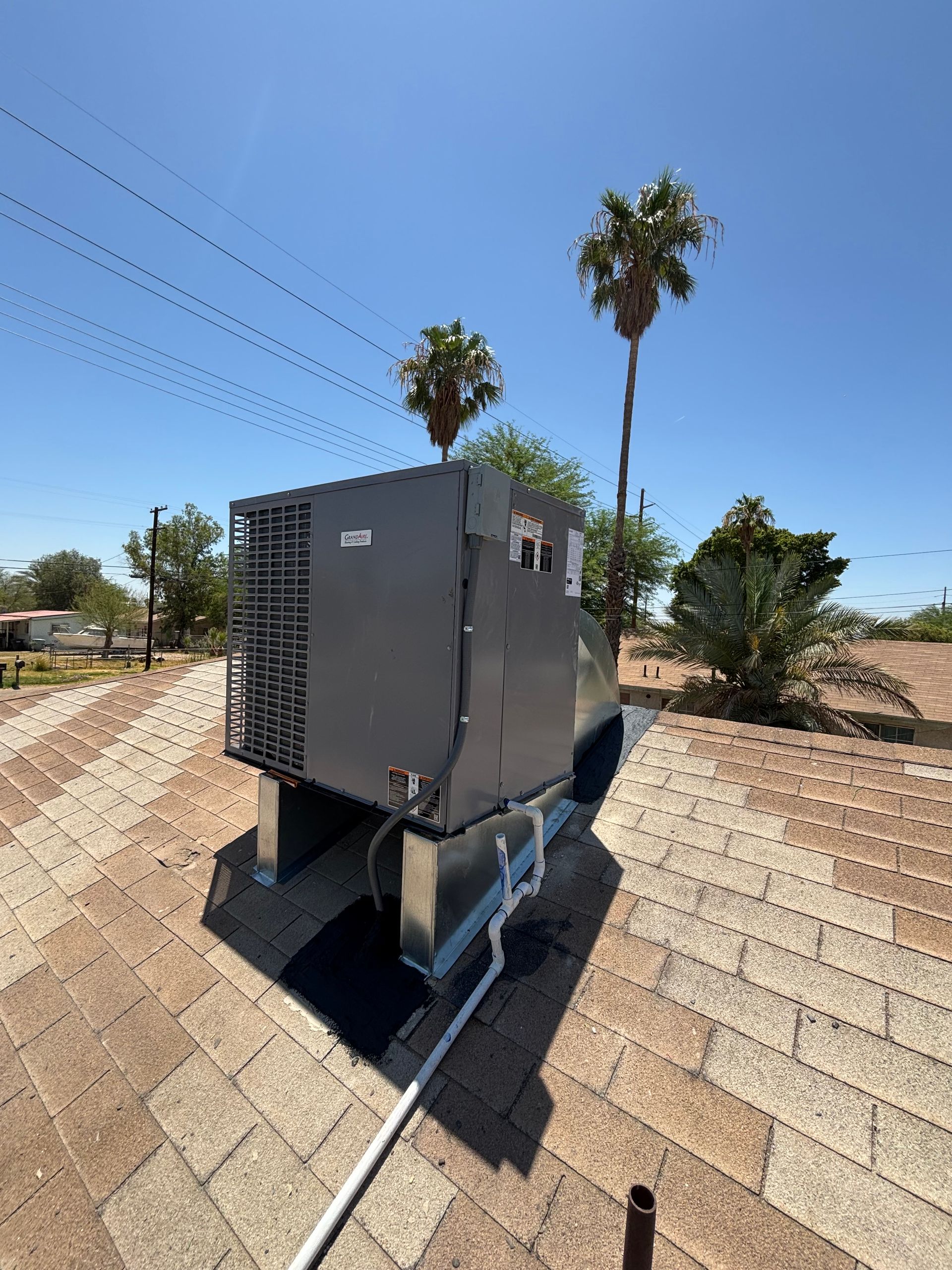 HVAC unit on a rooftop with palm trees in the background. Blue sky overhead.
