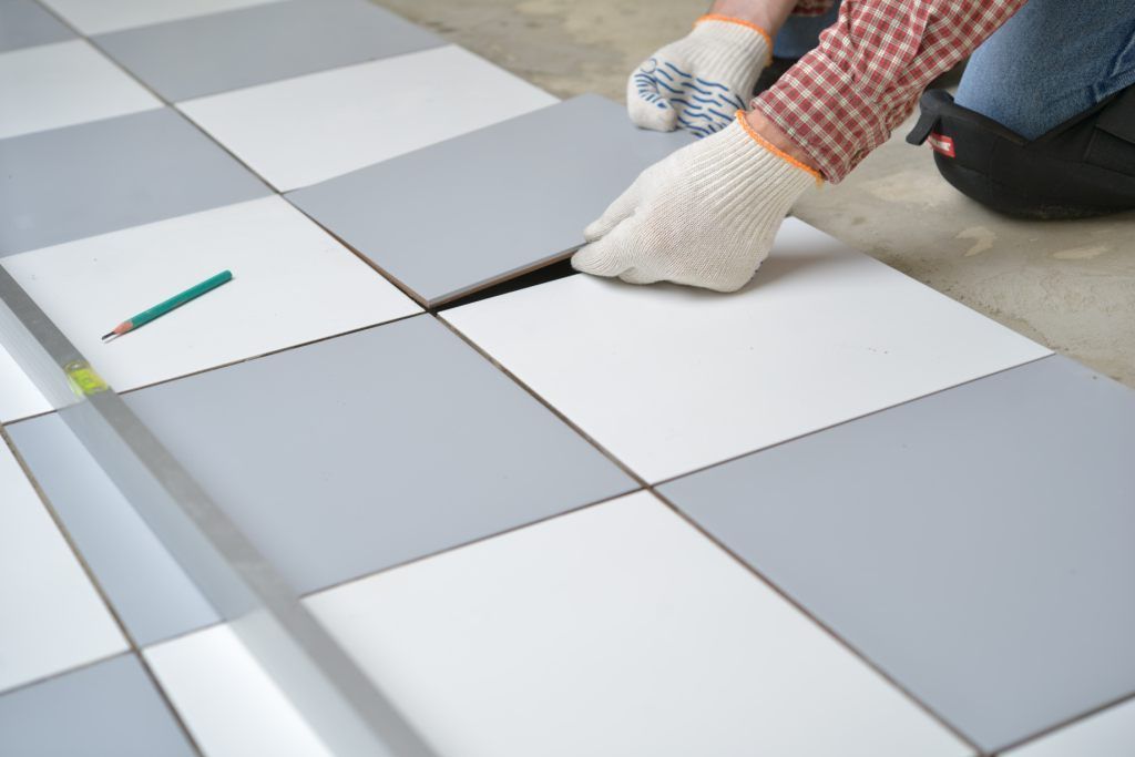 A person is laying tiles on a checkered floor.