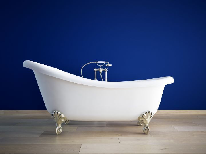 A white bath in front of a blue wall, on a wooden floor.