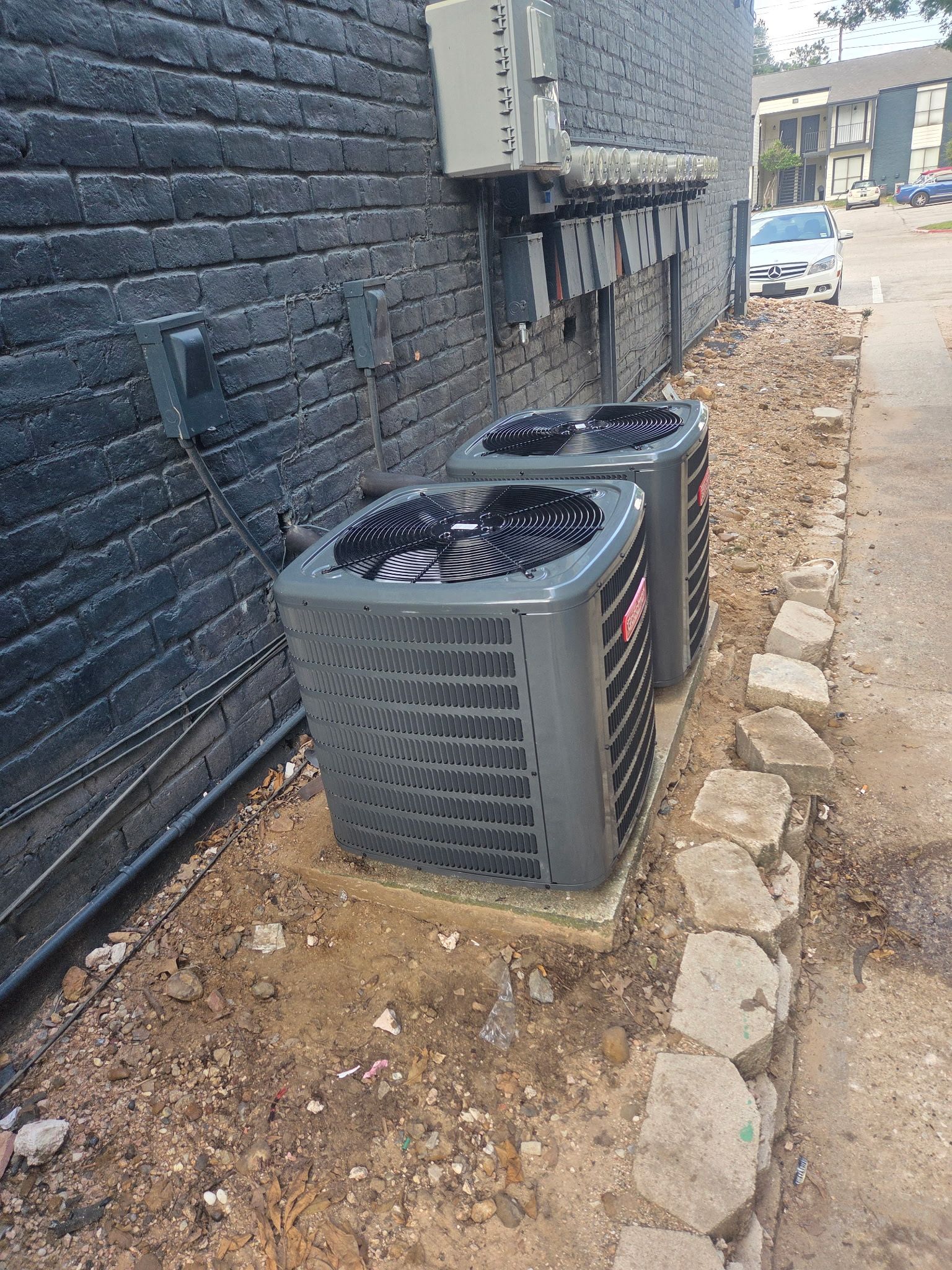 Two air conditioners are sitting on the side of a building next to a brick wall.