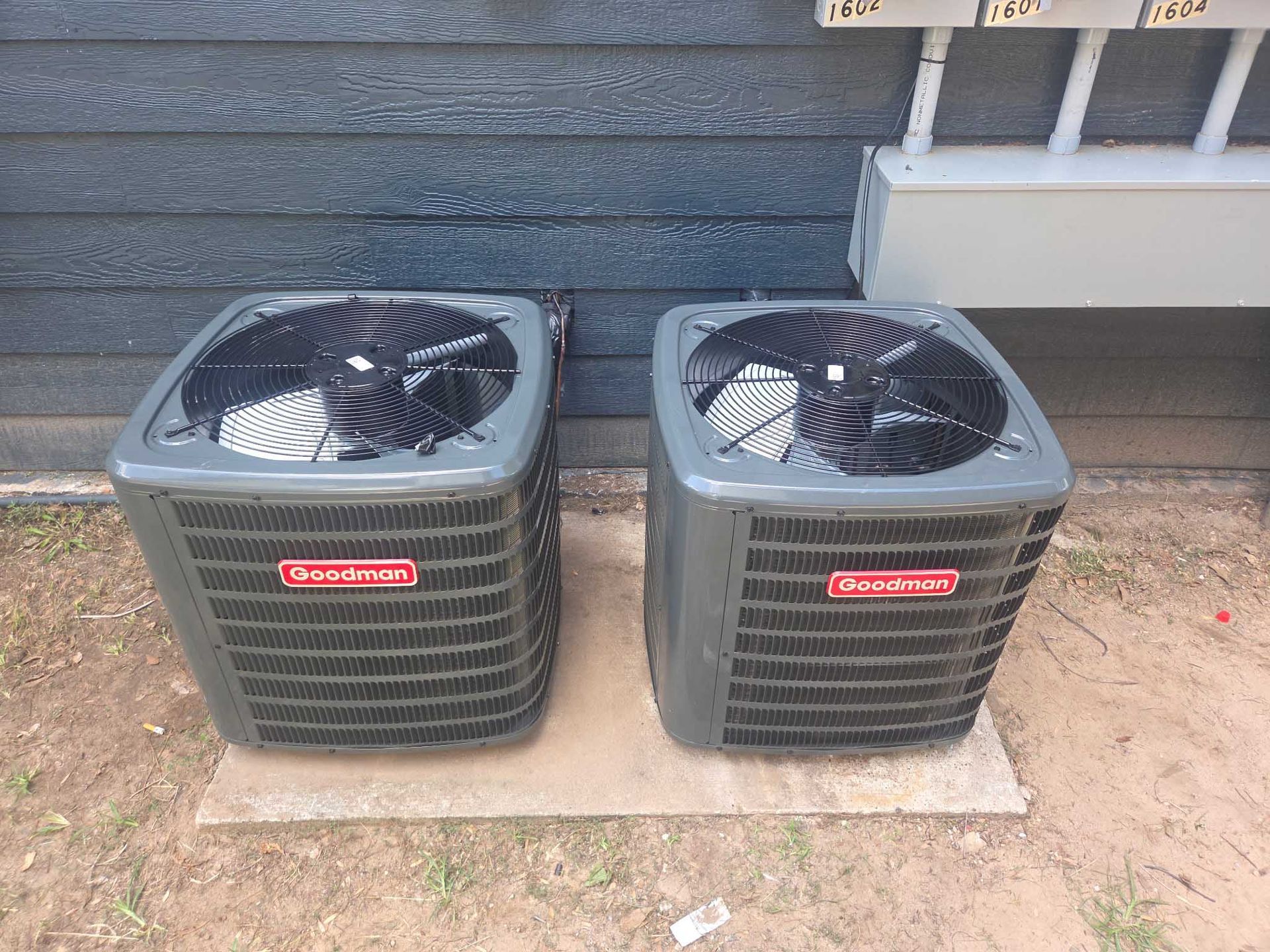 Two air conditioners are sitting next to each other on the ground in front of a building.