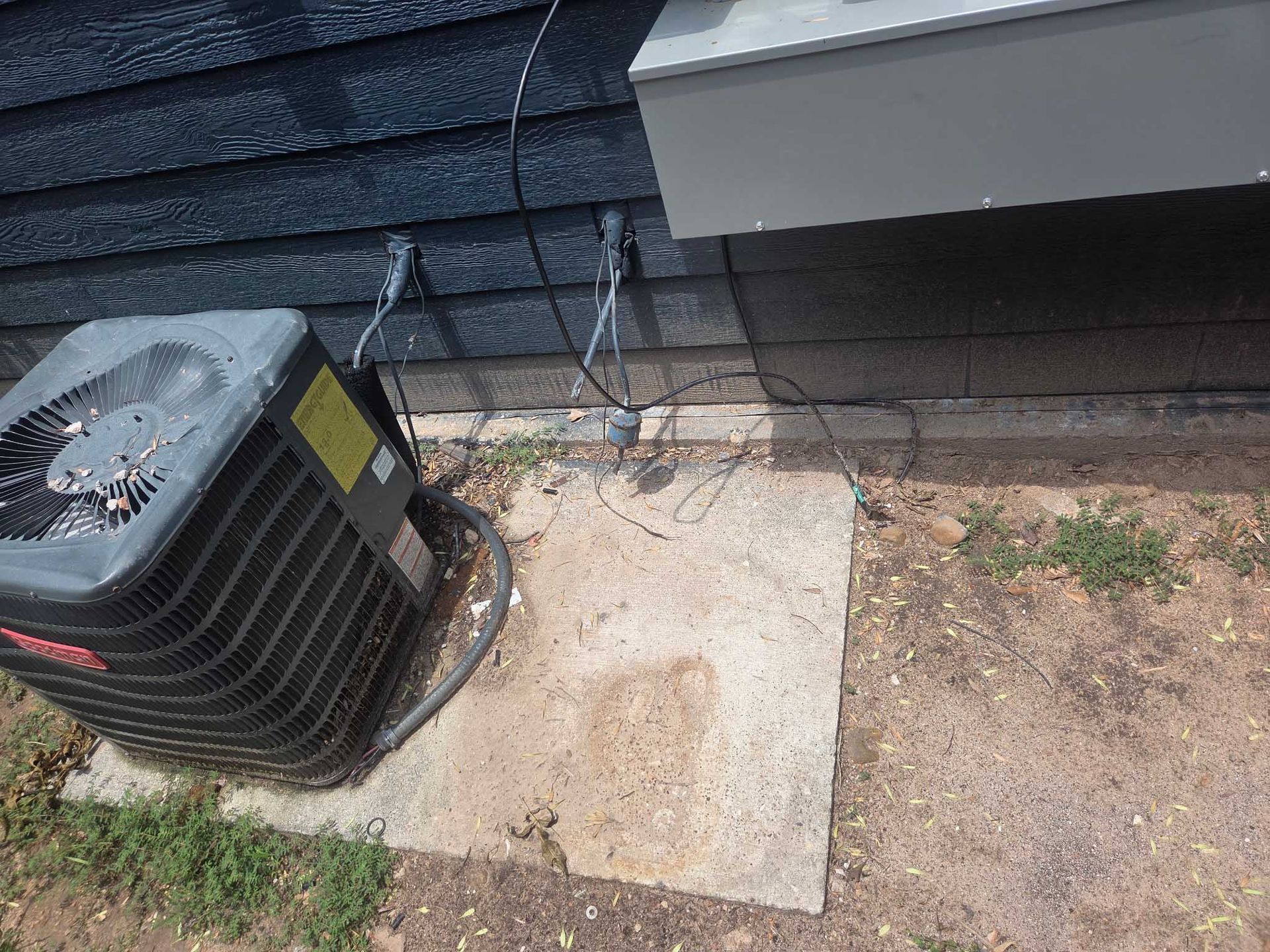 An air conditioner is sitting on the ground outside of a house.