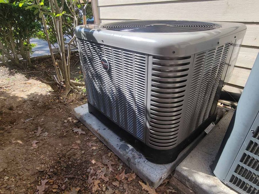 A large air conditioner is sitting on top of a concrete block next to a house.