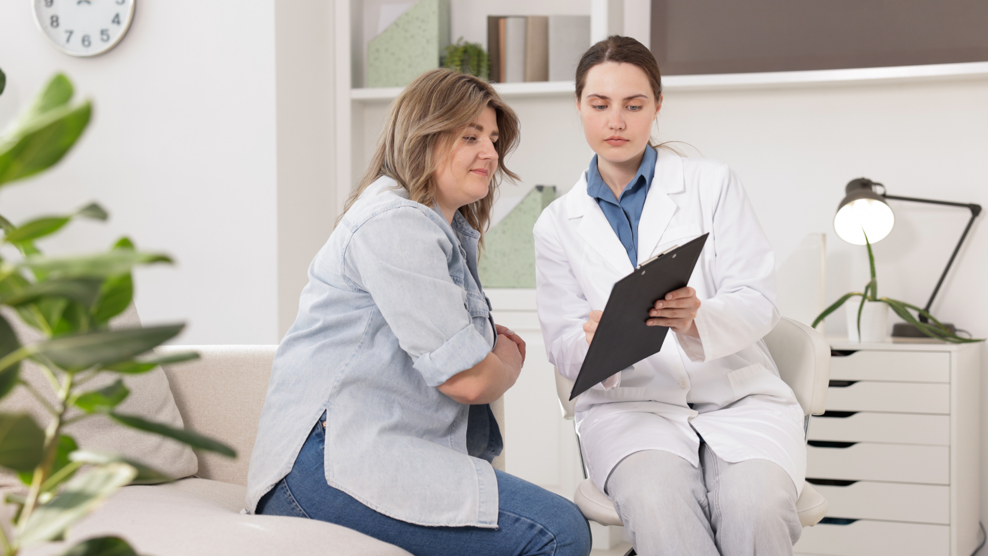 Doctor showing clipboard to patient on a couch in a well-lit office.