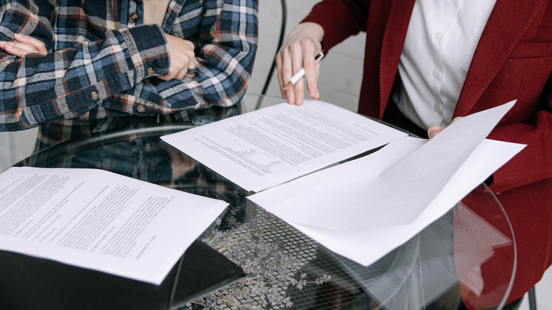 Man smiling, looking at a tablet, working at a kitchen table with a laptop, bills, and coffee.