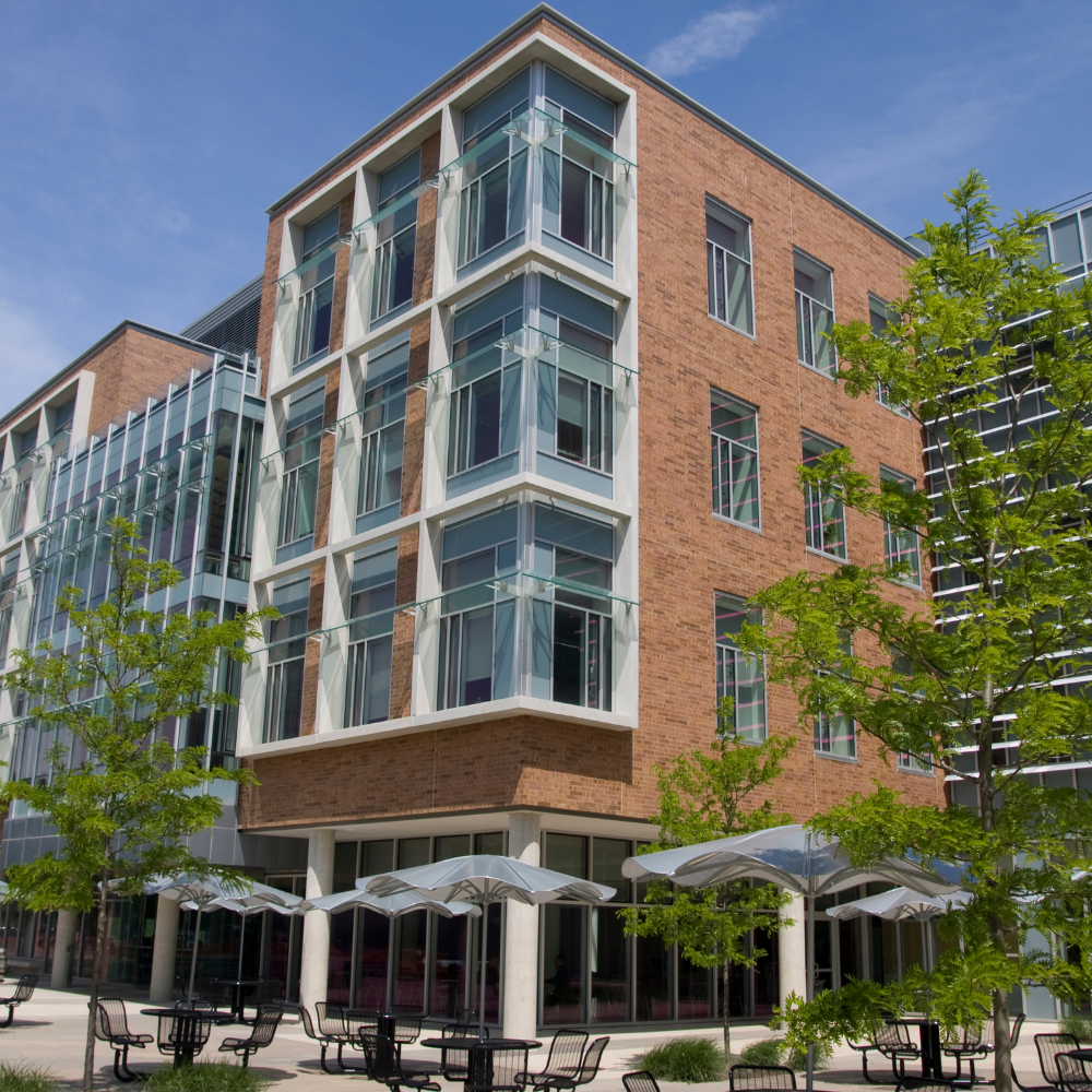 Brick and glass building with outdoor seating and trees under a blue sky.