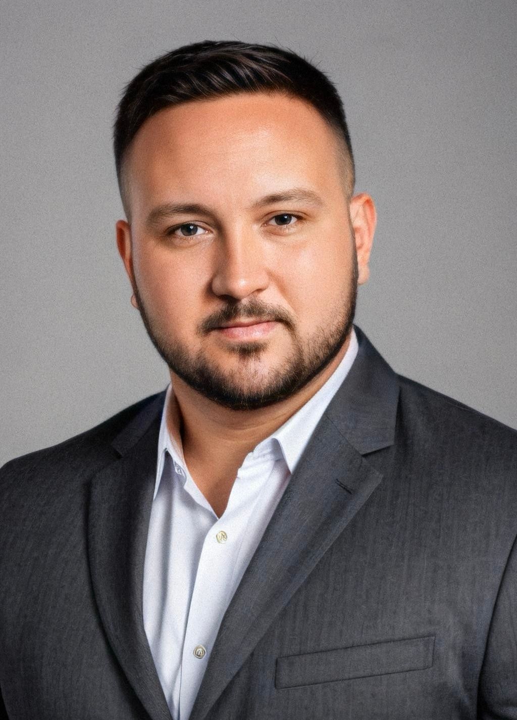 Man with a beard in a white shirt, working on a laptop with a glass of water nearby.