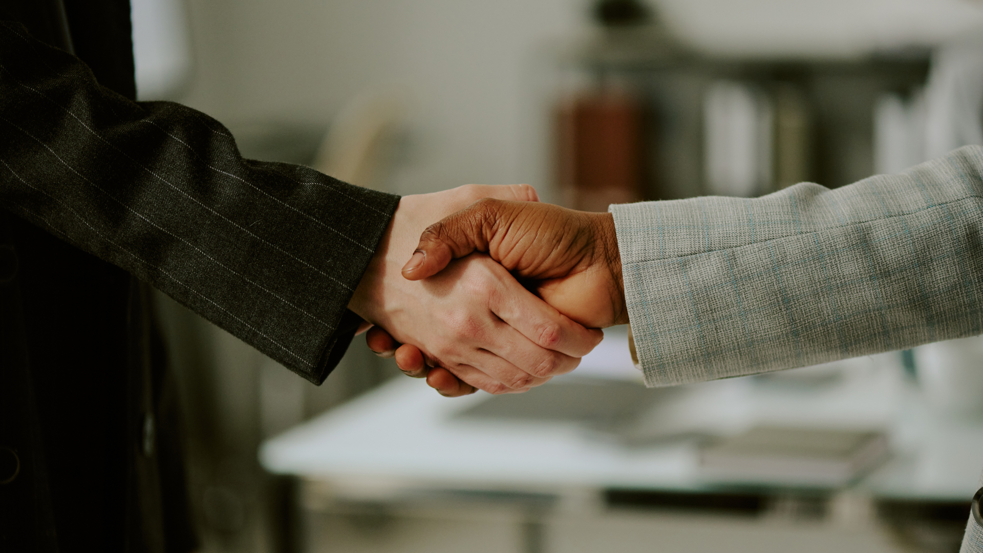 Two people shaking hands, one light-skinned, one dark-skinned, in an office setting.